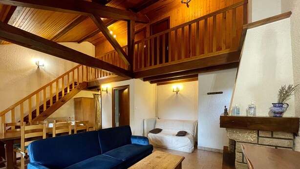 A spacious living area with a blue sofa, wooden table, and a staircase leading to an upper level.