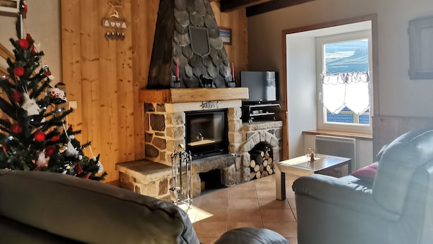 A cozy living room with a stone fireplace, wooden ceiling, and a Christmas tree.