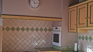 A kitchen with a gas stove, an oven, a clock, and wooden cabinets.
