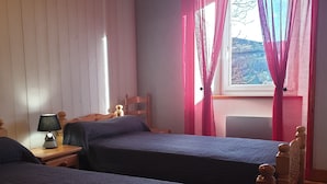 A bedroom with two beds, a nightstand with a lamp, a chair, and a window with curtains.