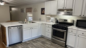 A modern kitchen with white cabinets, a stainless steel dishwasher, a gas stove, and a microwave.