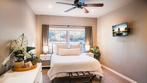 A bedroom with a bed, bedside tables, a ceiling fan, a window with curtains, a wall-mounted TV, and a potted plant. - Clean, Private Guesthouse-9 min. to Downtown Charleston, 15 min. to FollyBeach! (Charleston)