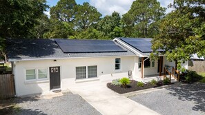 A single-story house with a white exterior, a dark roof, and solar panels on the roof.
