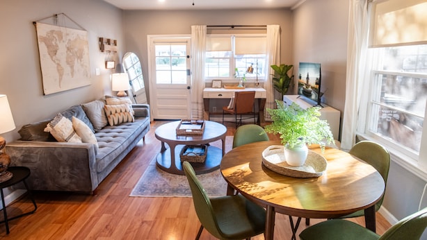 A modern living room with a grey sofa, a wooden coffee table, and a dining table with chairs. There is a ceiling fan, a world map on the wall, and a window with curtains. - Clean, Private Guesthouse-9 min. to Downtown Charleston, 15 min. to FollyBeach! (Charleston)