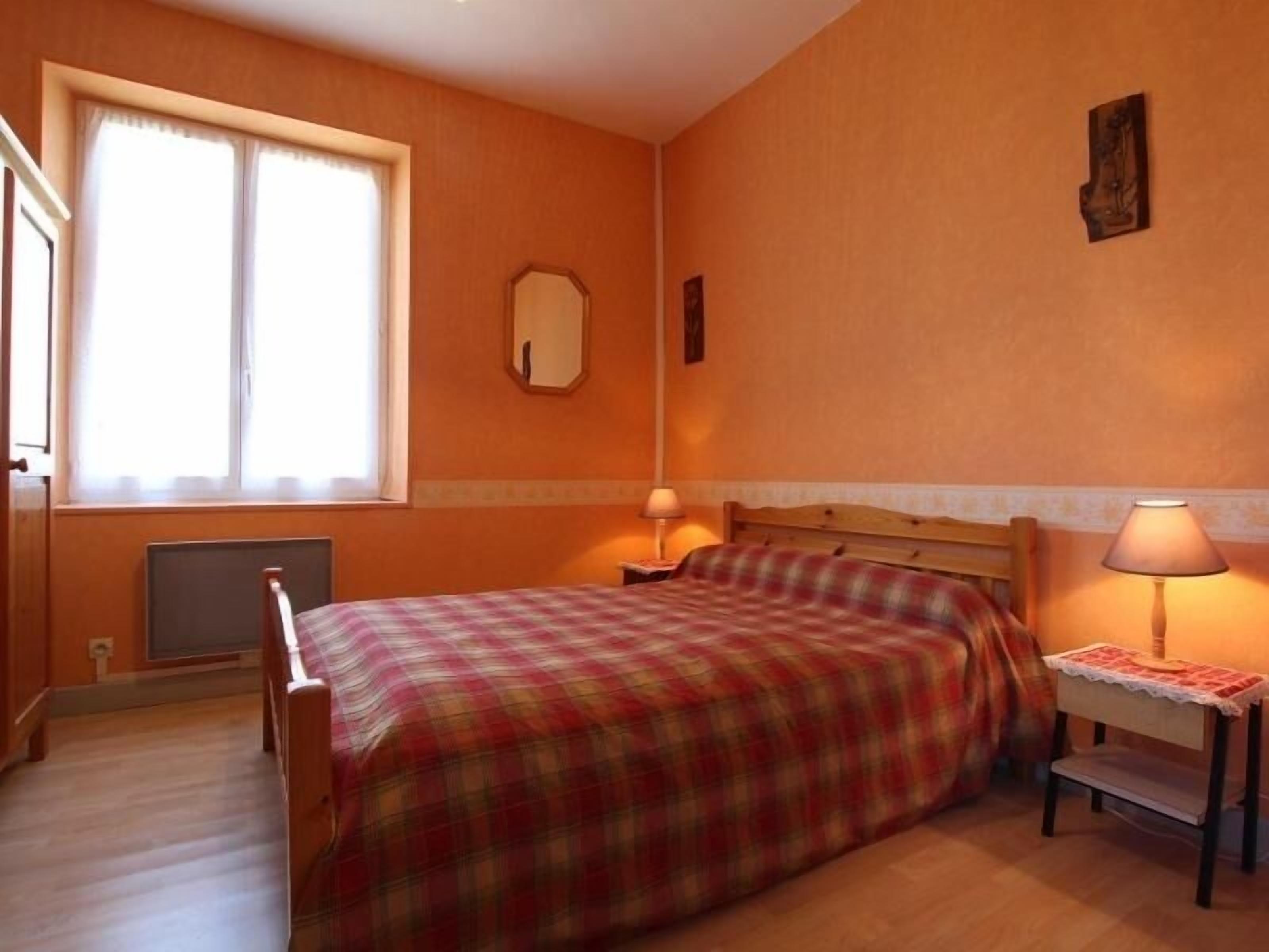 Une chambre à coucher comprenant un lit, une table de chevet, une lampe, une fenêtre et un miroir fixé au mur.
