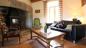 A cozy living room with a stone fireplace, a wooden table, a green armchair, and a black leather sofa. - Restored farmhouse with enclosed garden and terrace, near Puy en Velay (Le Monastier-sur-Gazeille)