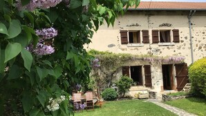 A stone building with a rustic facade, a small garden with a wooden table and chairs, and a pathway leading to the entrance. - Restored farmhouse with enclosed garden and terrace, near Puy en Velay (Le Monastier-sur-Gazeille)