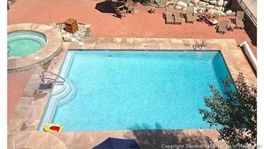 Une piscine avec un jacuzzi, des chaises longues et un mur en pierre.