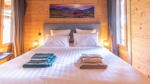 A wooden cabin bedroom with a bed, pillows, and towels. - Luxury Lodge with Private Spa, Golf Access, and Kids' Adventure Area (Le Chambon-sur-Lignon)