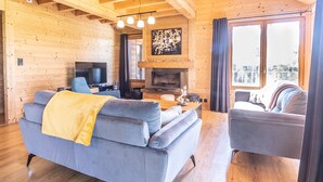 A cozy wooden interior with a sofa, armchair, and a fireplace. - Luxury Lodge with Private Spa, Golf Access, and Kids' Adventure Area (Le Chambon-sur-Lignon)