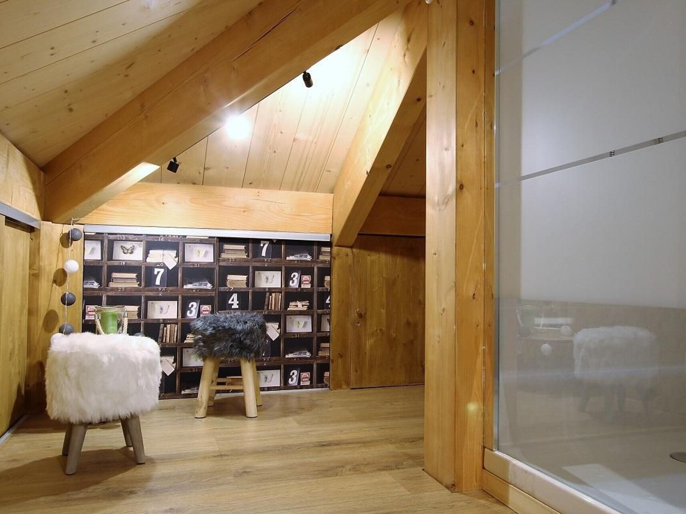 Une pièce mansardée chaleureuse avec des poutres en bois, un plafond en pente et une bibliothèque remplie d’objets encadrés.