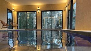 A modern indoor swimming pool with clear reflections, large windows, and a view of trees outside. - Luxury Lodge with Private Spa, Golf Access, and Kids' Adventure Area (Le Chambon-sur-Lignon)