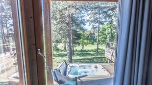 A hot tub on a wooden deck with a view of a grassy area and trees. - Luxury Lodge with Private Spa, Golf Access, and Kids' Adventure Area (Le Chambon-sur-Lignon)