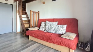 A room with a red sofa, patterned pillows, a wooden chair, a wooden staircase, and a wall-mounted deer head artwork. - Modern Apartment with Balcony, Mezzanine & Parking - Sleeps 6 (Bolquère-Pyrénées 2000)