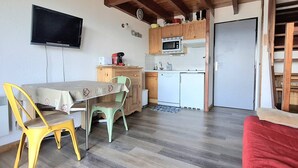 A compact kitchen with a microwave, stove, and sink. There is a dining table with chairs and a television mounted on the wall. - Modern Apartment with Balcony, Mezzanine & Parking - Sleeps 6 (Bolquère-Pyrénées 2000)
