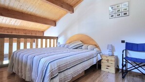 A bedroom with a wooden ceiling, a bed with striped bedding, a nightstand, a lamp, and a blue folding chair. - Modern Apartment with Balcony, Mezzanine & Parking - Sleeps 6 (Bolquère-Pyrénées 2000)