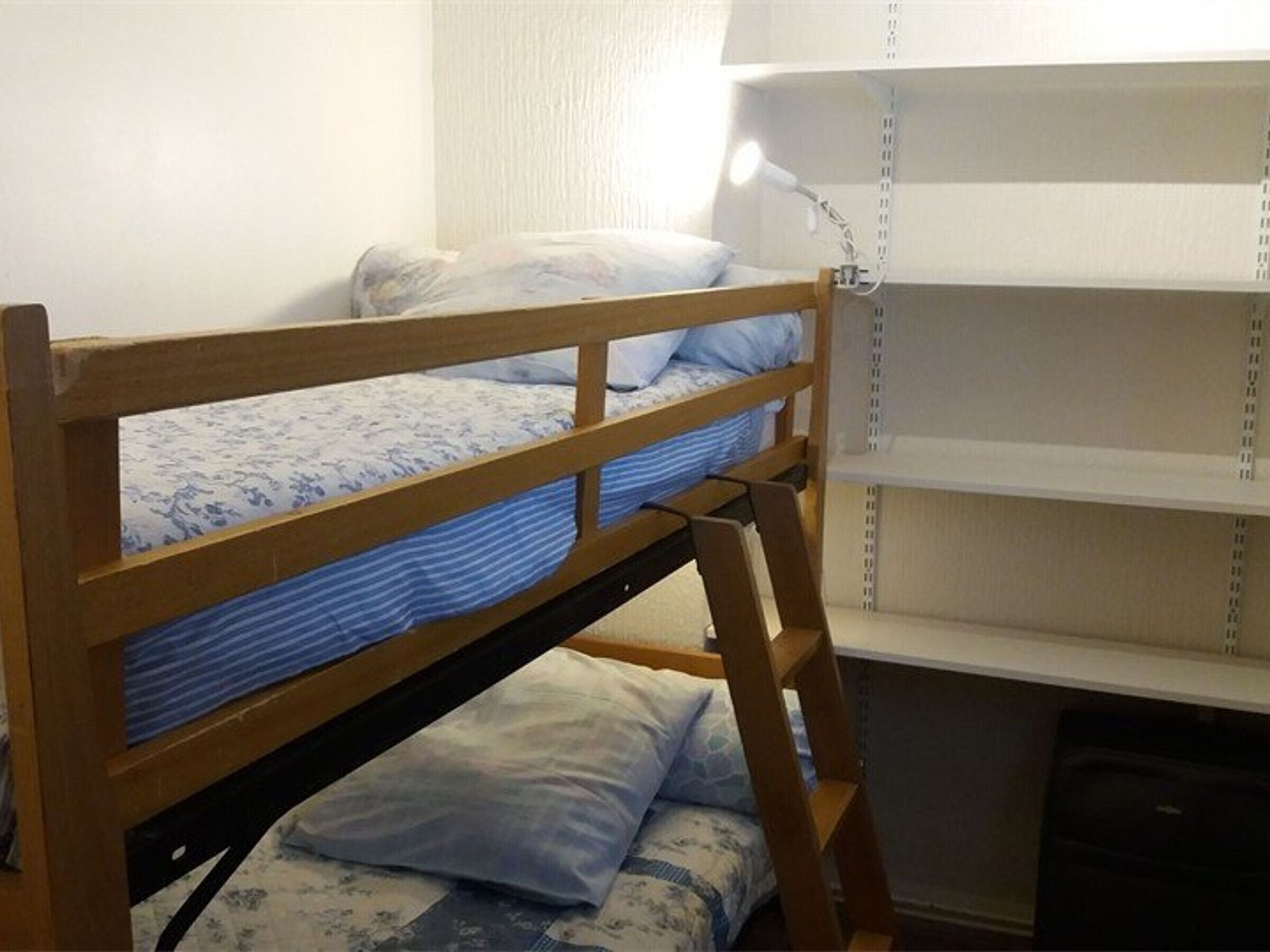 A bunk bed with a wooden frame, a desk with a lamp, and a window with blinds.