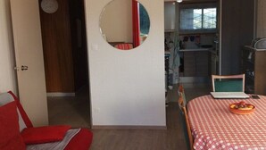 A room with a bed, a round mirror, a dining table with a checkered tablecloth, and a laptop. - Cozy 2-Room Apartment with Cabin for 6, Near Shops and 800m from Ski Slopes (Bolquère-Superbolquère)