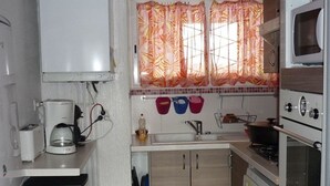 A compact kitchen with a microwave, stove, and sink. There are cabinets below the countertop and a small window with curtains. - Cozy 2-Room Apartment with Cabin for 6, Near Shops and 800m from Ski Slopes (Bolquère-Superbolquère)