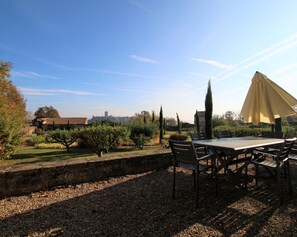 Patio esterno con tavolo e sedie, circondato da ghiaia e vegetazione, con vista sulla città.