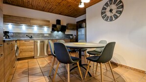 A modern kitchen with wooden cabinets, a stainless steel dishwasher, and a dining area with a round table and four chairs. - Cottage with private terrace and garden in Saugues, all inclusive (Saugues)