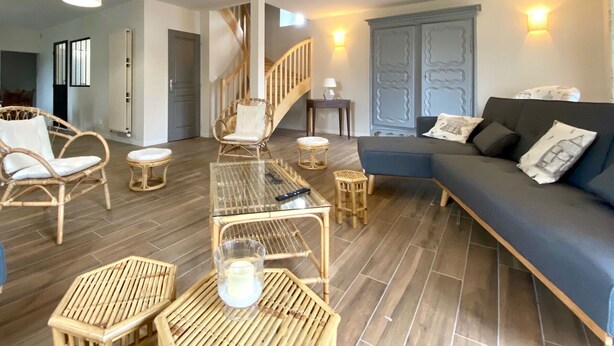 Ein modernes Wohnzimmer mit Treppe, Korbmöbeln, einem blauen Sofa und einem Glastisch.