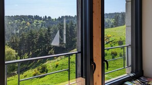Una habitación con un ventanal grande que da a un paisaje verde con árboles y una estructura distante.