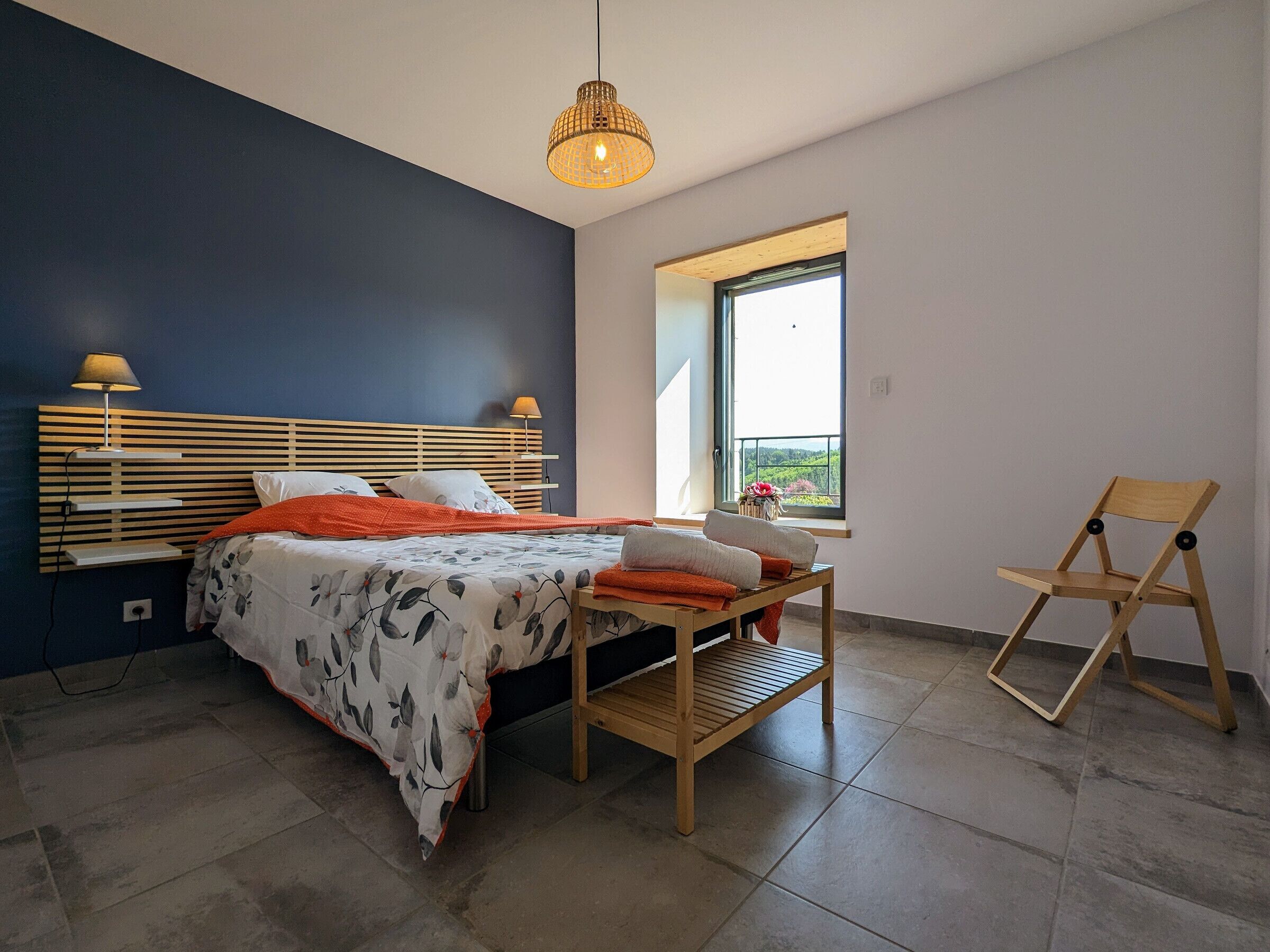 A modern bedroom with a bed, bedside lamps, a wooden chair, and a window with a view.