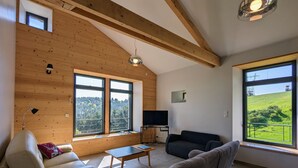 Una sala de estar con techo de madera, ventanas amplias, un sofá, una mesa de centro y una televisión.