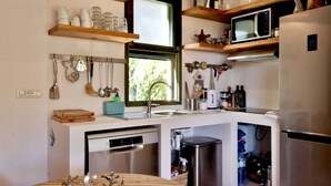 Eine kompakte Küche mit Geschirrspüler, Mikrowelle und Spüle. Über der Arbeitsplatte befinden sich Holzregale mit Tassen und Gläsern.