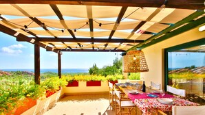 Ein Essbereich im Freien mit Tisch für zwei Personen, einer Pergola darüber und Blick auf das Meer.