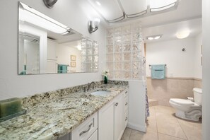 A bathroom with a granite countertop, a sink, a toilet, and a glass shower enclosure.