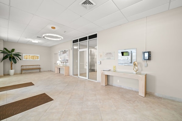 A modern reception area with a glass door entrance, a reception desk, a potted plant, and a bench.