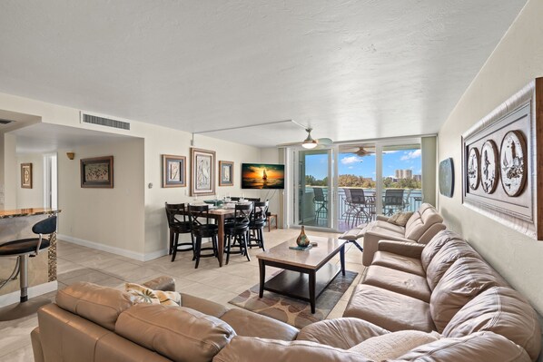 A spacious living room with a large sofa, a dining area with chairs, and a TV mounted on the wall.