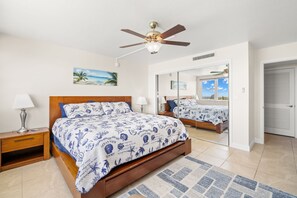 A bedroom with a wooden bed, a ceiling fan, a nightstand, a lamp, a mirror, and a view of the outside.