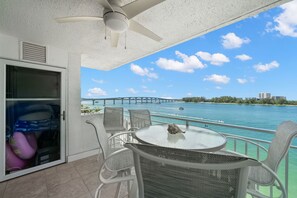 A balcony with a glass table, wicker chairs, and a view of a bridge over water.