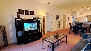 Un salon comprenant un téléviseur, un canapé, une table basse et un coin repas avec des chaises et une table.