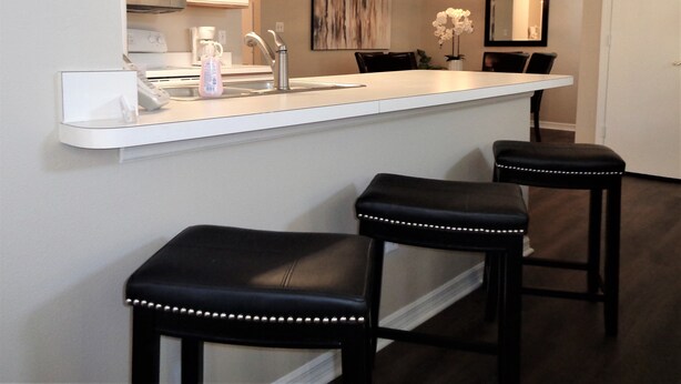 A modern kitchen with a white countertop, stainless steel appliances, and two black bar stools.