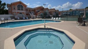 A swimming pool area with lounge chairs and a building with multiple windows and a staircase.