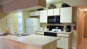A compact kitchen with white cabinets, a black microwave, a stove, and a sink. - Family-Friendly 1st Floor Poolside Condo | 3BR/2BA | 5 Miles to Disney! (Kissimmee)