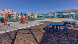 A playground with swings and tables, surrounded by buildings with balconies. - Family-Friendly 1st Floor Poolside Condo | 3BR/2BA | 5 Miles to Disney! (Kissimmee)