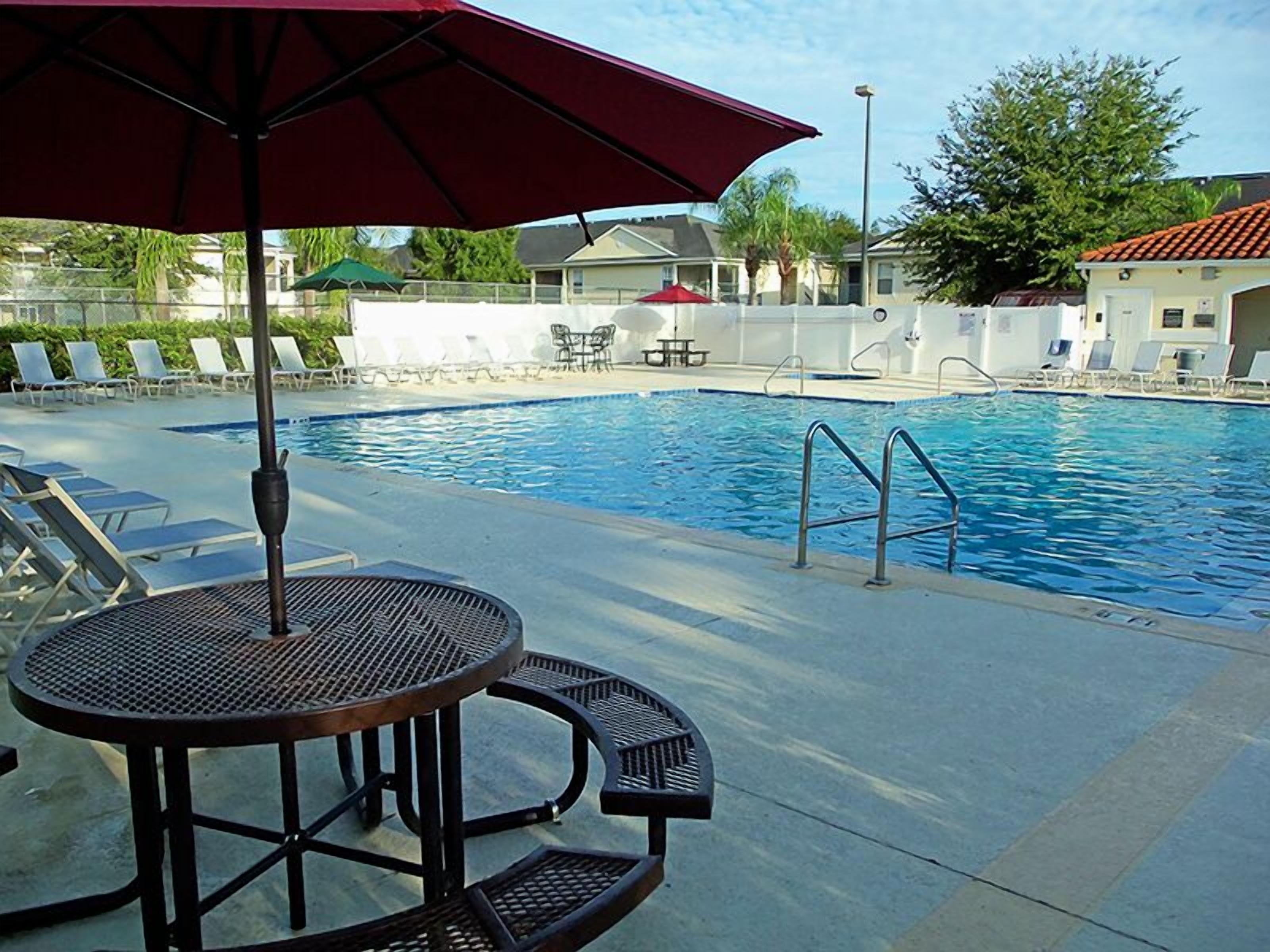 Piscina com espreguiçadeiras e mesa com guarda-sol.