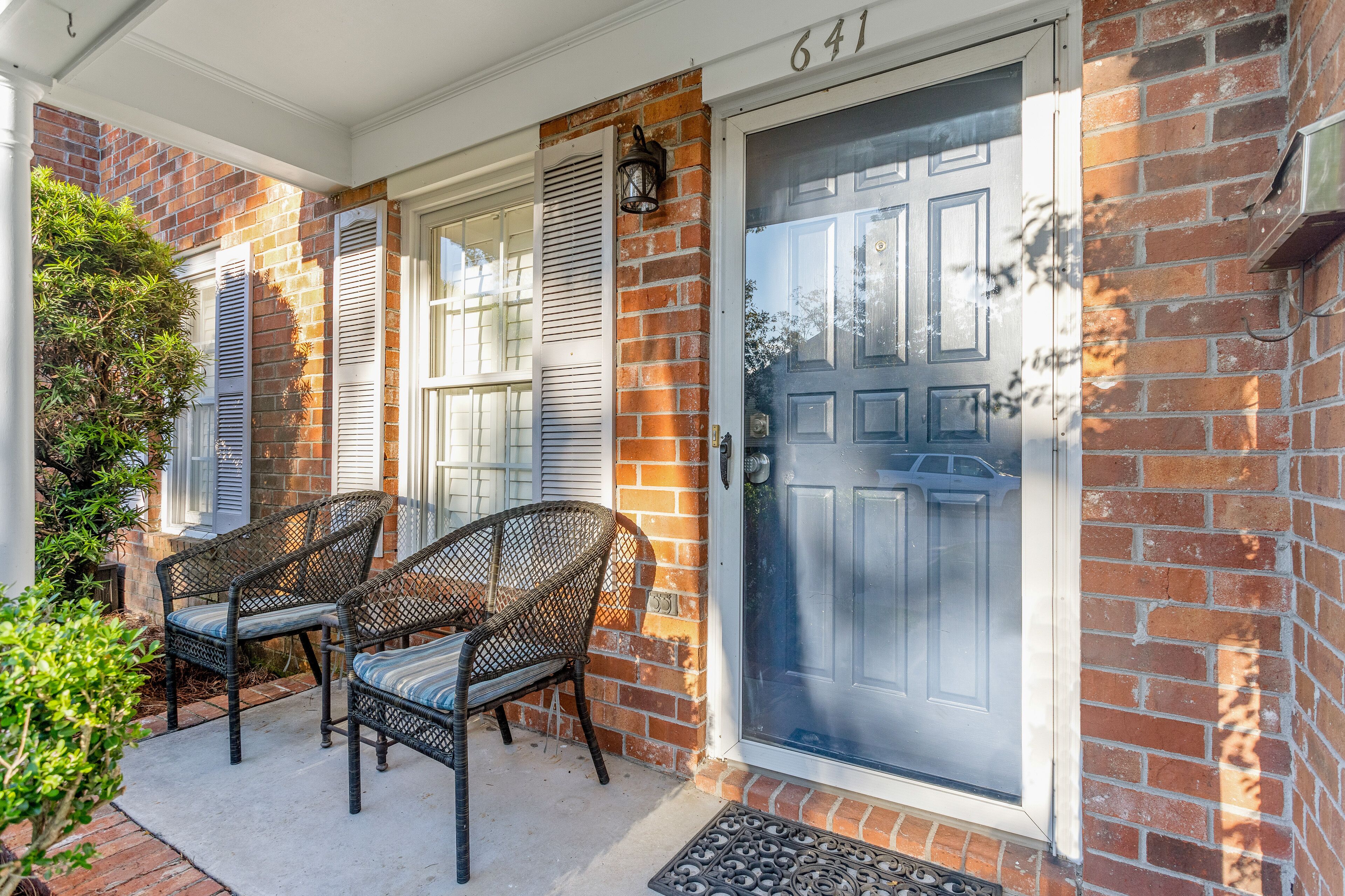 A brick house with a blue door, two wicker chairs, and a small porch area.