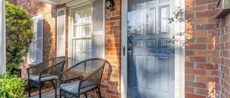 A brick house with a blue door, two wicker chairs, and a small porch area.