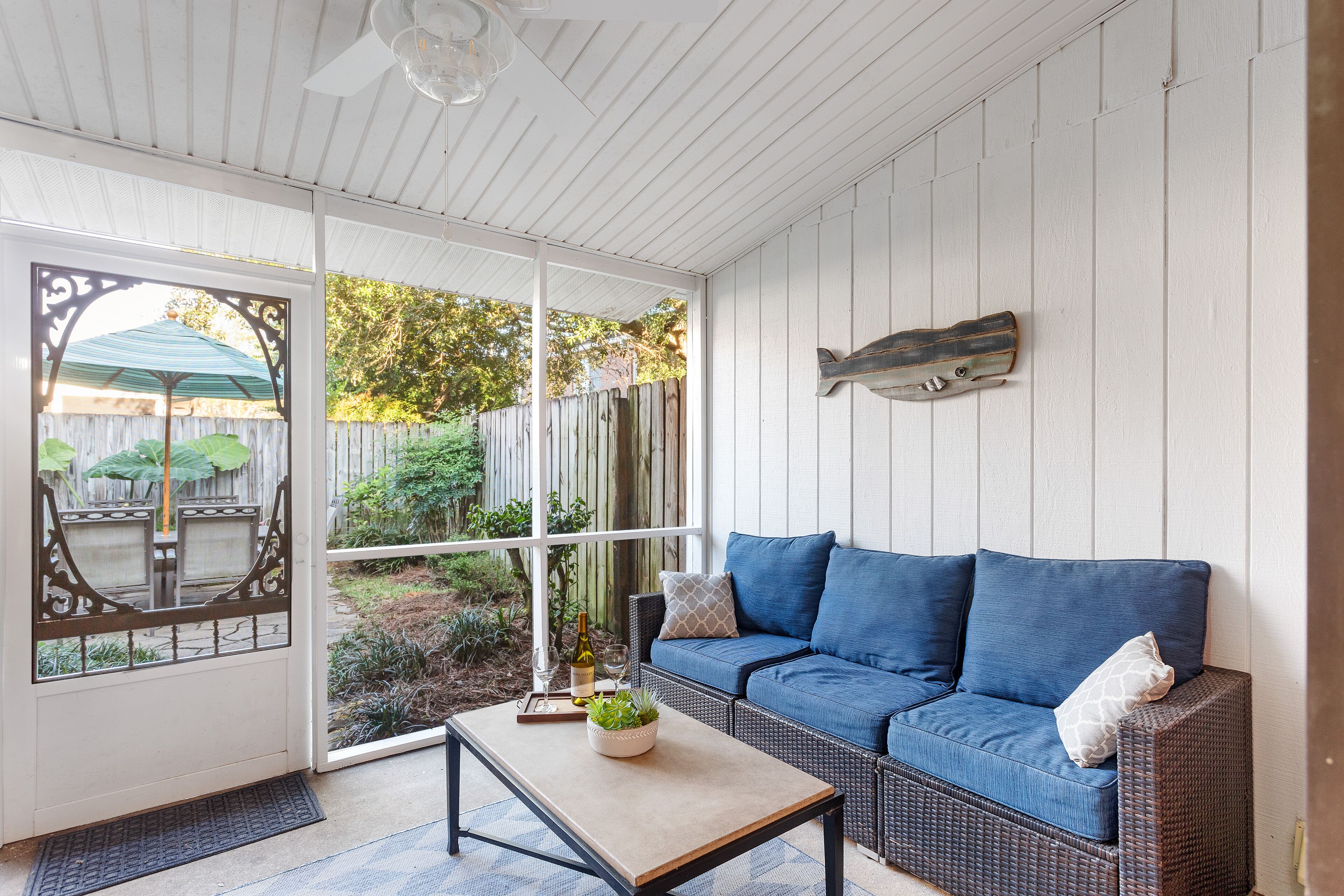 A covered patio area with a wicker sofa, a small table with a plant, and a decorative fish mounted on the wall.