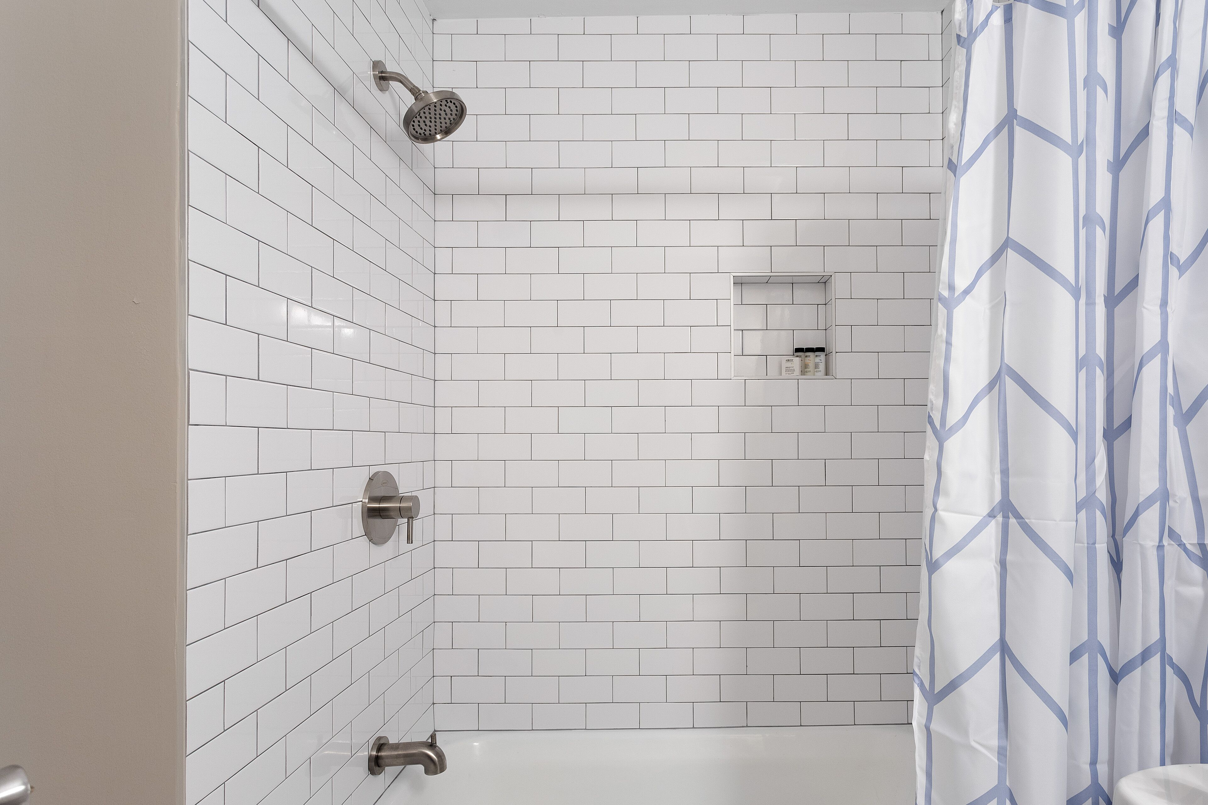 Un baño con azulejos blancos tipo metro, ducha e inodoro.