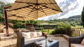 An outdoor patio with wicker furniture, a glass table, and a large umbrella. - Luxury-Villa, Tuscany-Villa, Private Swimming Pool-Villa (Panzano In Chianti)