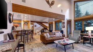 A spacious living area with a wooden ceiling, a cozy sofa, a coffee table, and a dining area with a bar.