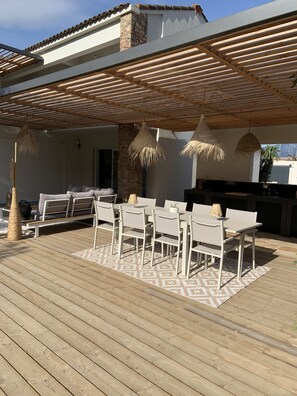 Eine Außenpatio mit Holzterrasse, einem Esstisch mit Stühlen, einer hängenden Leuchte und einer Steinwand.