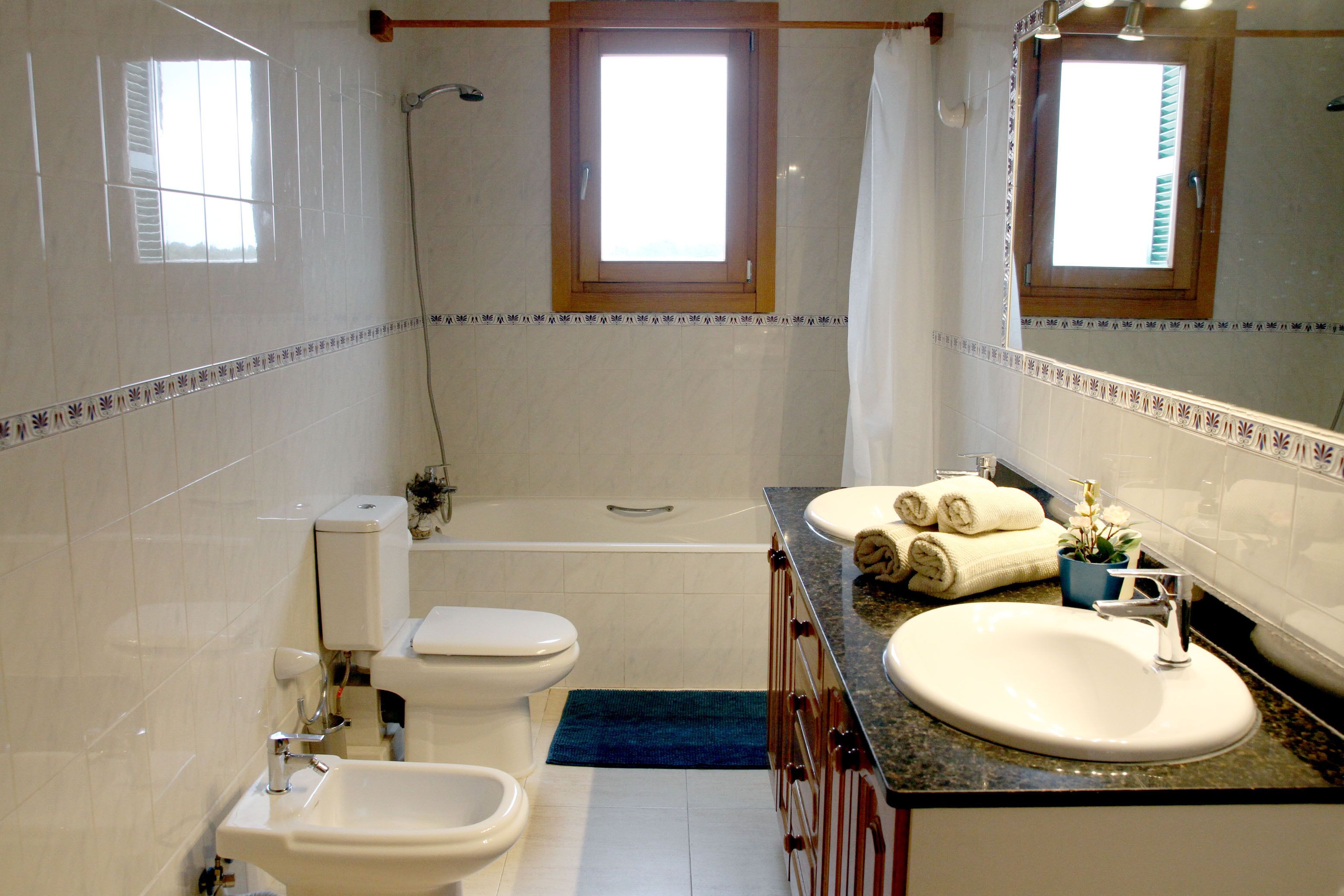 A bathroom with a toilet, bidet, sink, and bathtub. There are windows and a shower curtain.